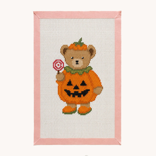A framed cross-stitch design featuring a teddy bear dressed as a pumpkin holding a lollipop, with a pink stitched border and a white studio background. The brand name 'Studio Daisy' is visible at the bottom.