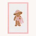 A needlepoint canvas design featuring a brown teddy bear wearing a pink and white striped swimsuit and a pink hat, holding a pink striped towel. The design is framed by a pink border on a white canvas, set against a light beige background with the 'STUDIO daisy' logo at the bottom.