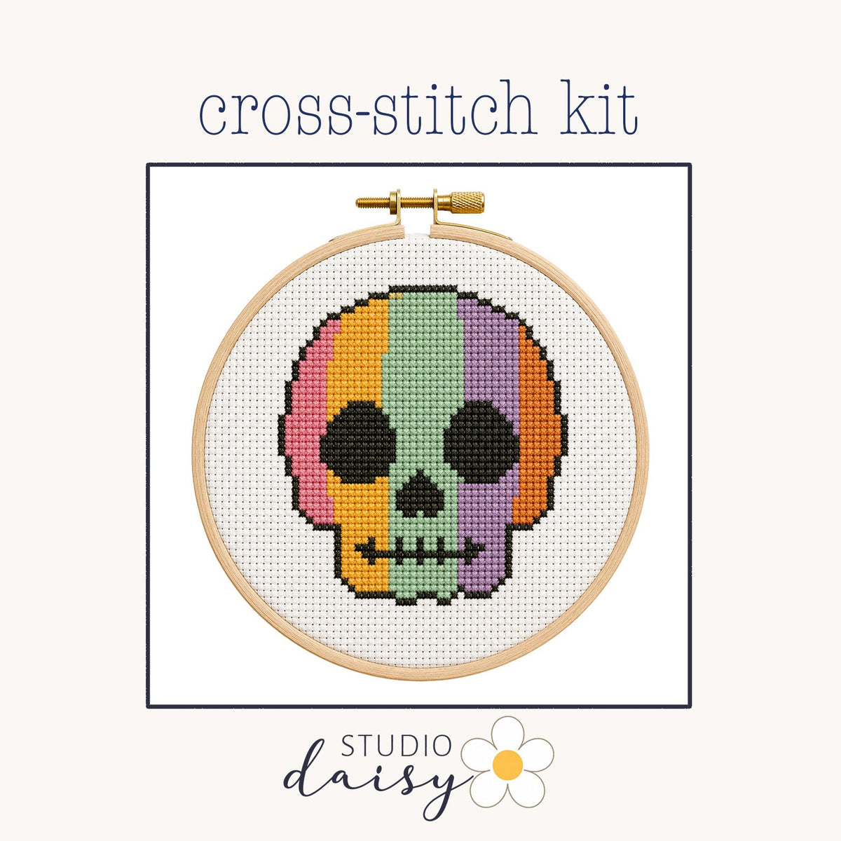 A cross-stitch kit preview showing a colorful skull design stitched inside a wooden embroidery hoop on a light cream background, with the text 'cross-stitch kit' above and 'STUDIO daisy' below.